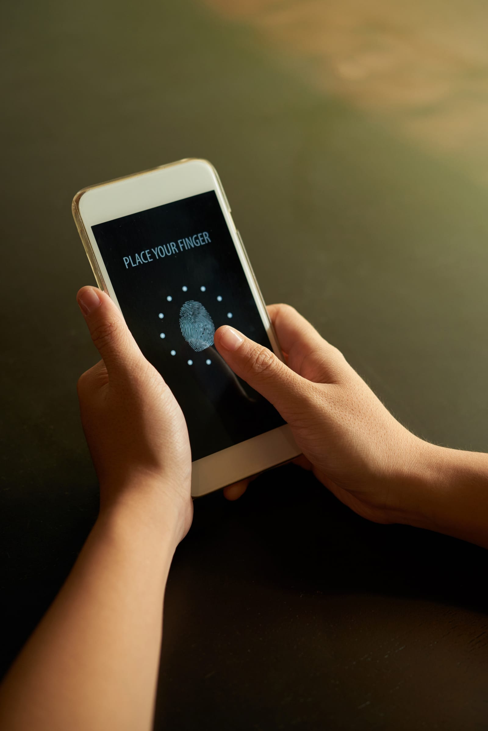 Duas mãos seguram um celular exibindo a solicitação de impressão digital em tela escura de desbloqueio.