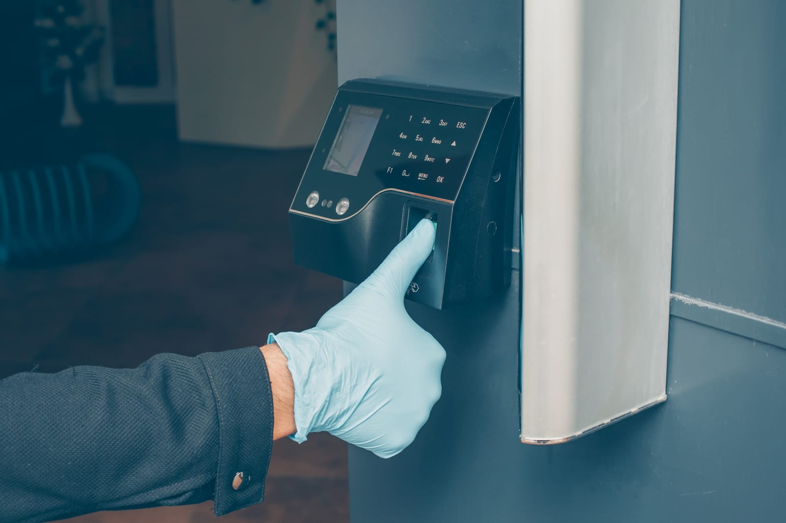 Um dedo enluvado pressiona o sensor de um terminal de acesso biométrico instalado na parede.