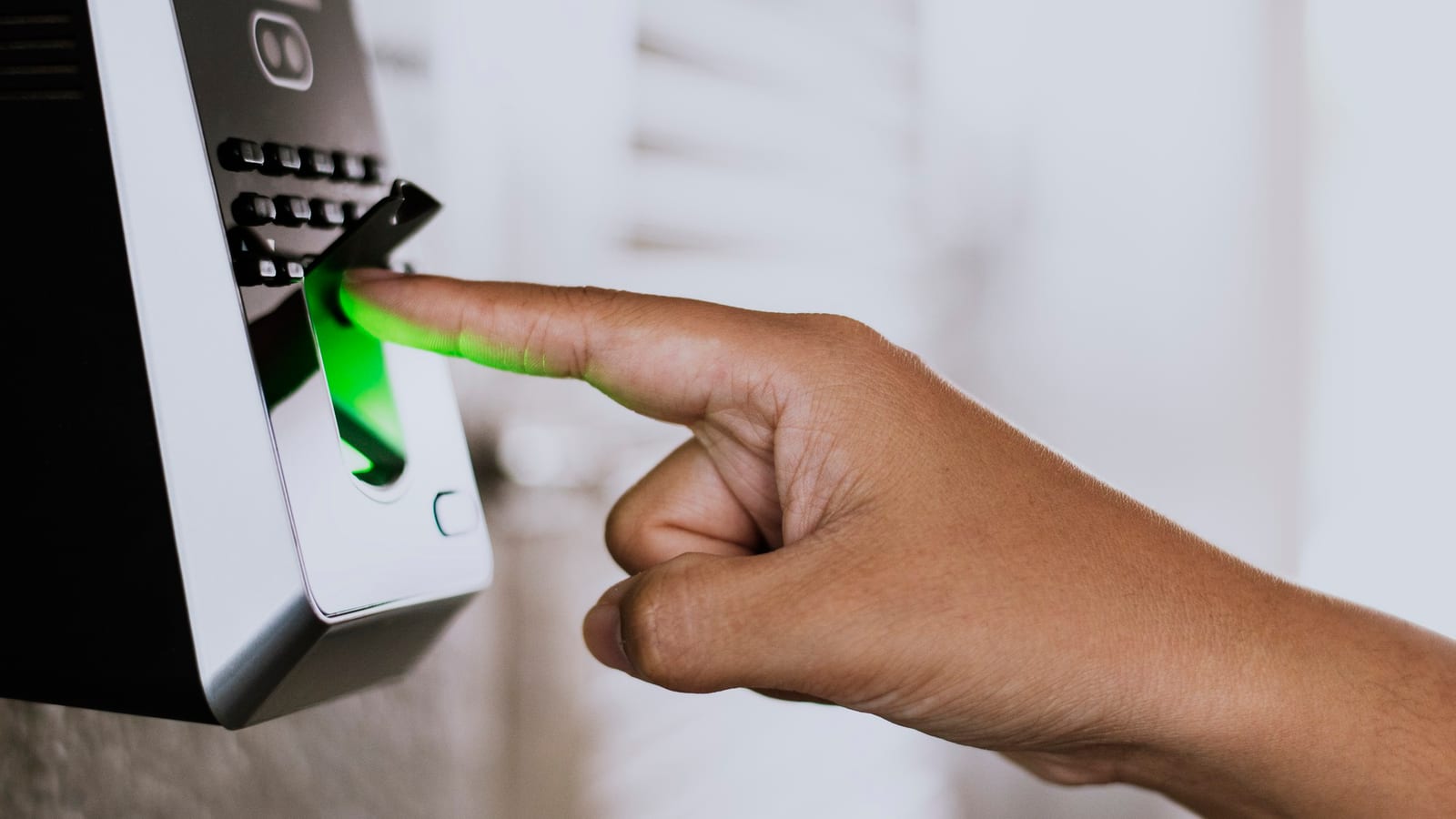 Um dedo repousa sobre o sensor iluminado em verde de um leitor de impressão digital.