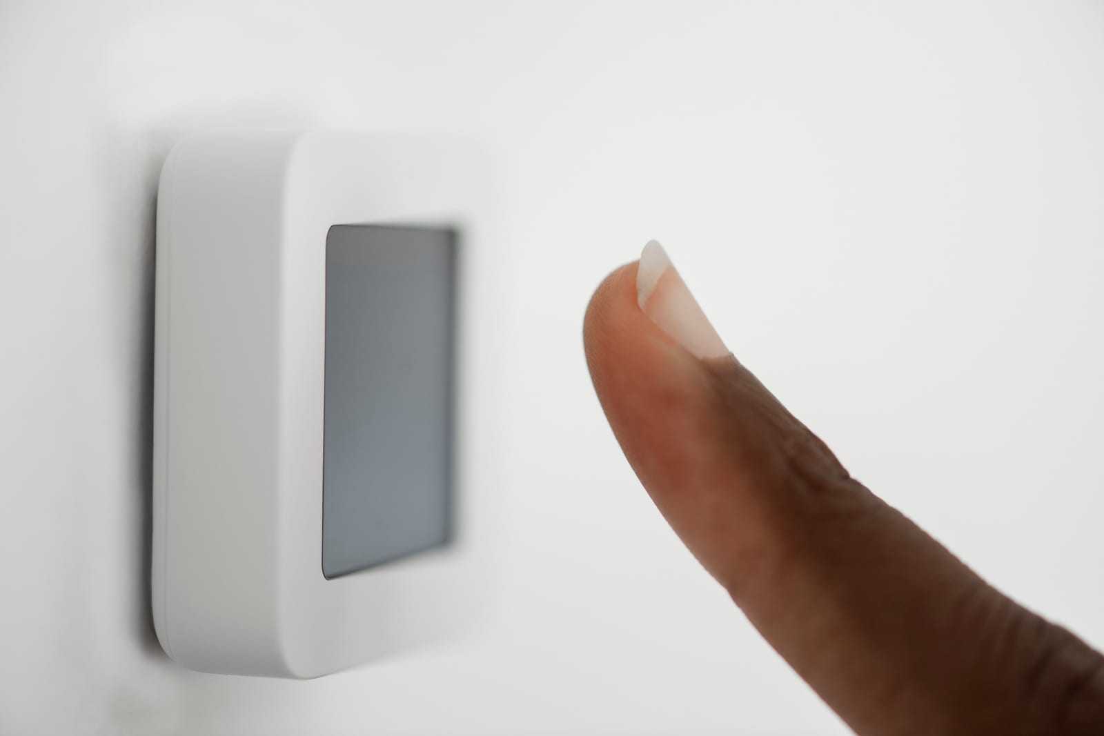 Um dedo se aproxima de um pequeno terminal touch branco fixado na parede.